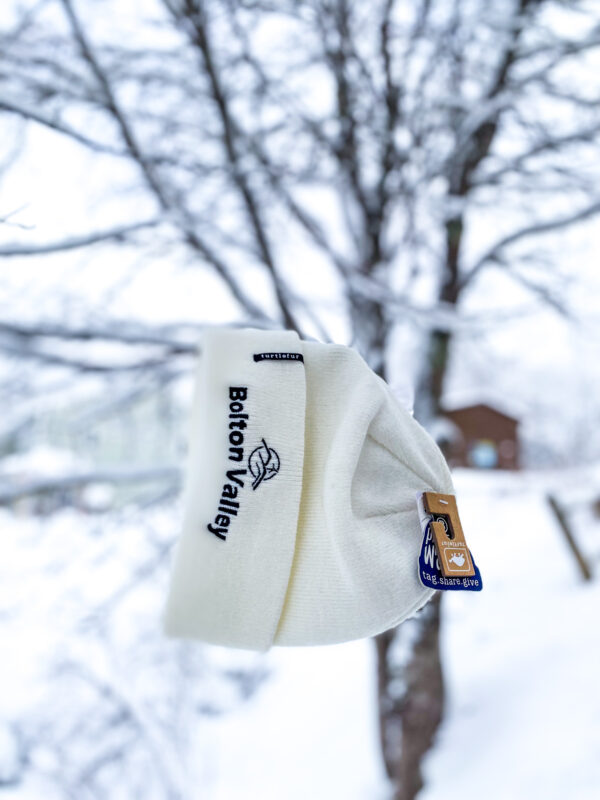 White embroidered beanie that reads "Bolton Valley" hanging from a snow covered tree
